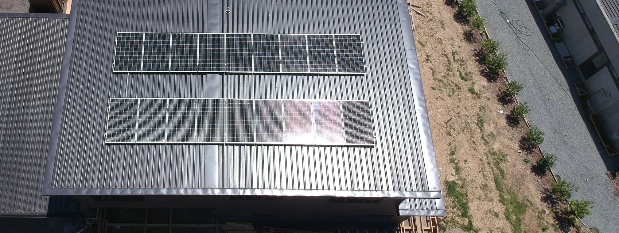 Aerial view of two rows of solar panels on a dark metal roof